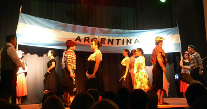 fotografía escenario chicos bailando folclore con una bandera argentina de fondo